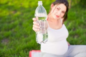 dehydration-during-pregnancy-Pregnant woman-outside-holding-water-bottle-grass | American Pregnancy Association